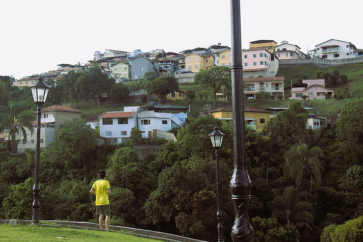 Menino de costas, com camiseta amarela e bermuda verde, observa casas na encosta do morro.