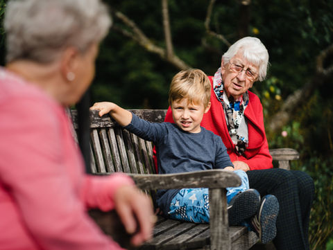 Zwei ältere Damen sitzen mit einem kleinem Jungen auf einer Parkbank