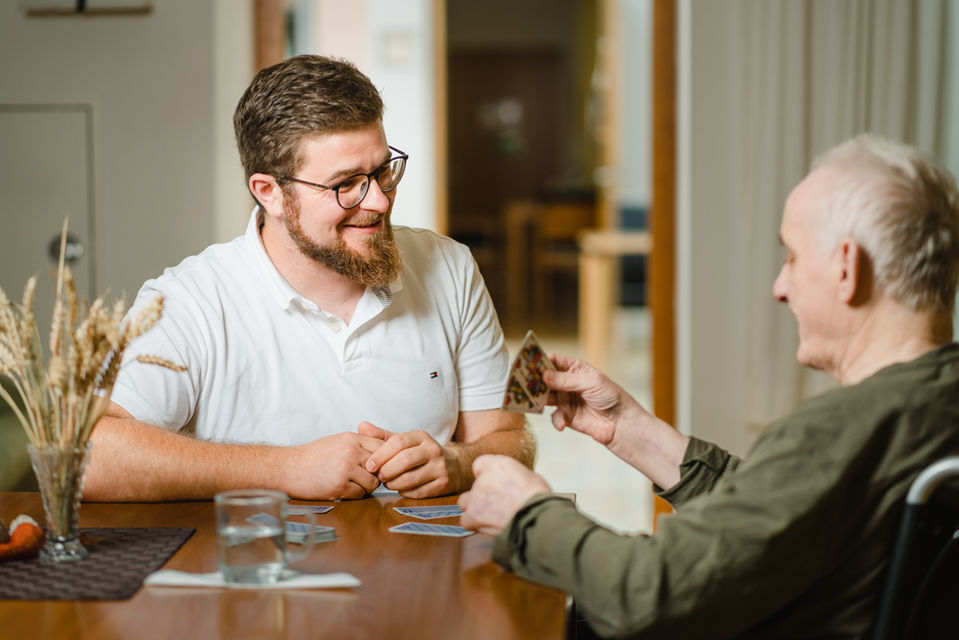Ein Pfleger spielt mit einem älteren Herren Karten