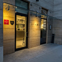 Restaurant entrance with "STAND" sign, warm lighting, glass doors, Michelin 2025 and Dom Perignon signs. Stone facade, evening setting.