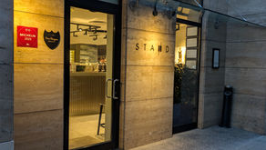 Restaurant entrance with "STAND" sign, warm lighting, glass doors, Michelin 2025 and Dom Perignon signs. Stone facade, evening setting.