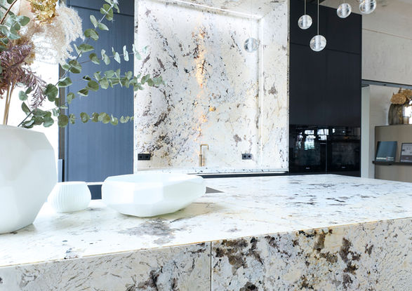 Neue Ausstellungsküche im Küchenatelier Hamburg: Transluzenter Granit ‘White Tiger’ mit hinterleuchteter Rückwand und Echtholzfronten in Davos. Die massive Insel kombiniert Licht, Struktur und natürliche Materialien zu einem modernen Küchen-Statement.