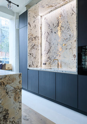 Neue Ausstellungsküche im Küchenatelier Hamburg: Transluzenter Granit ‘White Tiger’ mit hinterleuchteter Rückwand und Echtholzfronten in Davos. Die massive Insel kombiniert Licht, Struktur und natürliche Materialien zu einem modernen Küchen-Statement.