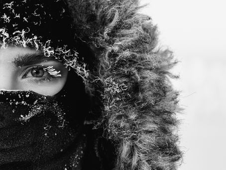 Nahaufnahme eines weiblichen Gesichts mit Sturmhaube und flauschiger Kapuze mit Fellbesatz im Winter in schwarz-weiß