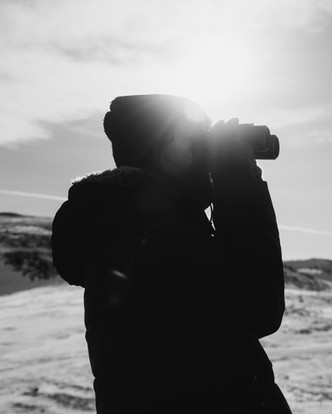 Black-and-white side view of a man looking through binoculars.