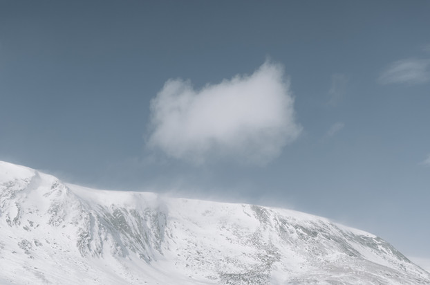 Snow-covered mountainside beneath a blue sky with a single cloud.