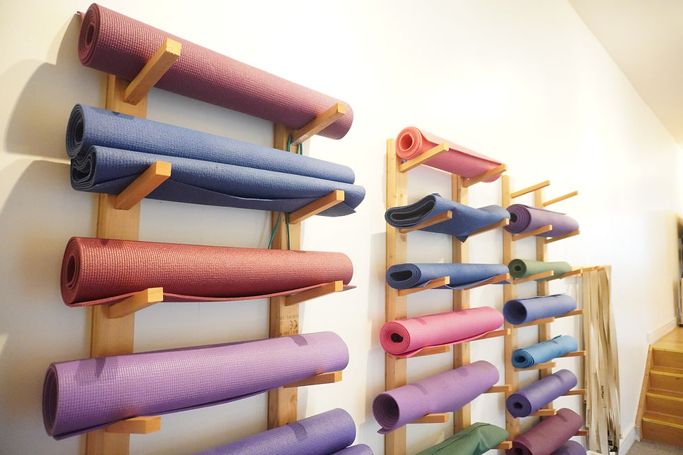 Storage rack with neatly arranged colourful yoga mats against a white wall.