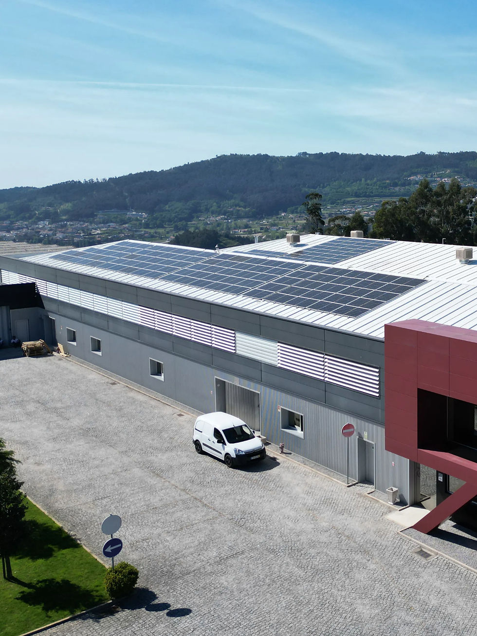 Industrial building with solar panels on the roof, a white van parked outside. Green hills and a clear blue sky in the background.