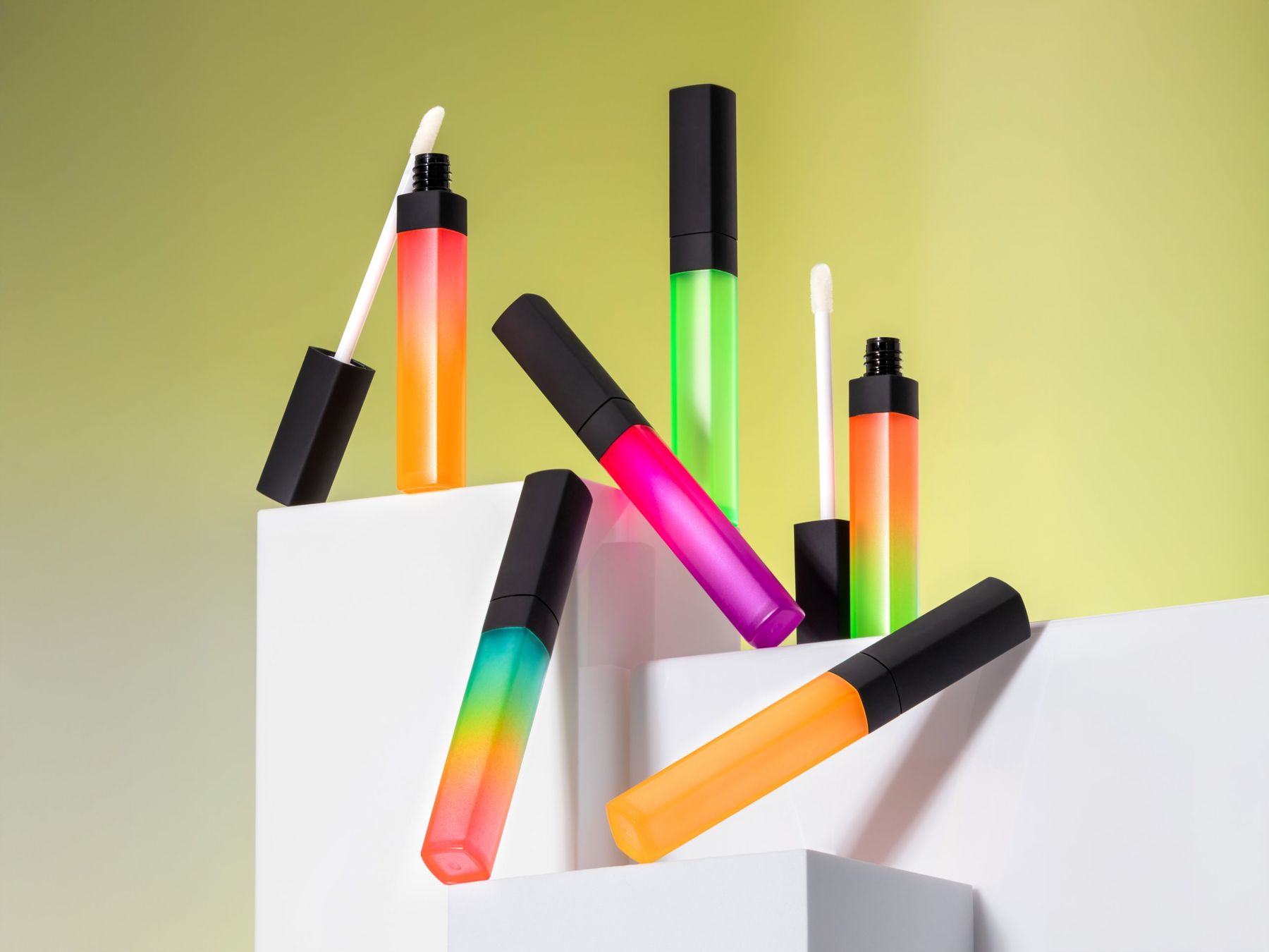 Colorful lip gloss tubes styled on white blocks