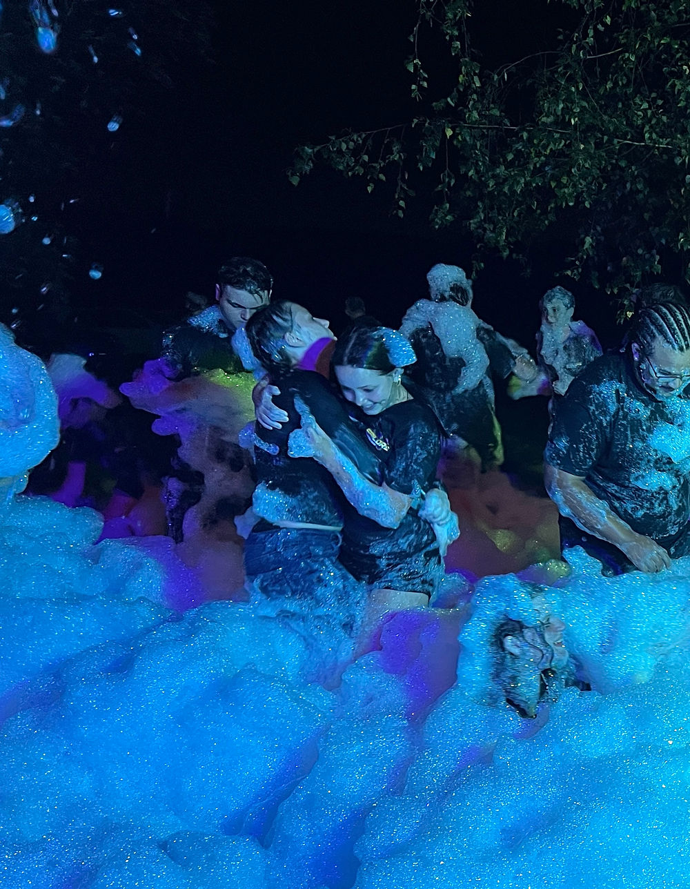 high school kids having an evening party in a pile of foam, illuminated by party lights