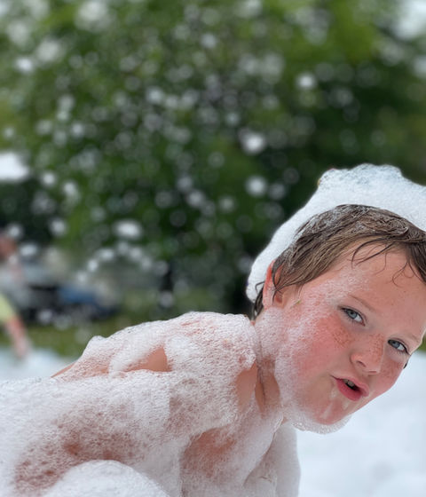 A boy “swimming” in the foam, grinning at the camera