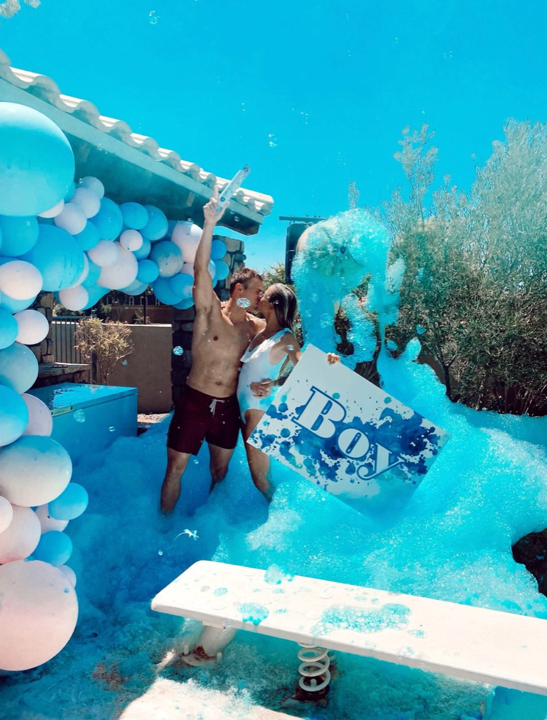 a happy couple embraces, surrounded by blue foam and holding up a simple sign that says "boy"