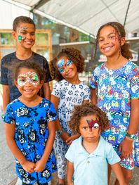 Group of children smiling with colorful custom face painting designs including butterfly, superhero, fantasy, and Minecraft-inspired artwork, created by Grand Creations by JE at a Tampa Bay event.