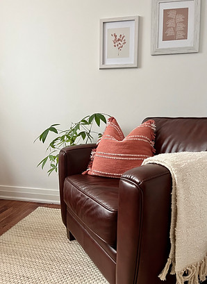 Embodied Healing's therapy and wellness office space with hanging art, a chair, pillow, blanket and plant