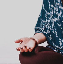 Female sitting in a meditation position, crossed legged with her hand in a mudra, placed on her knee