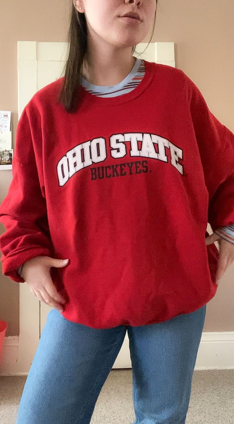 Fall outfit with a red crewneck, jeans, and a long-sleeved shirt.