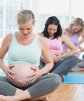 Pregnant women sitting on mats touching their bumps