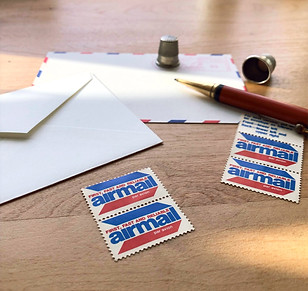 Envelopes, airmail stamps, a pencil, and two thimbles lying on a desk