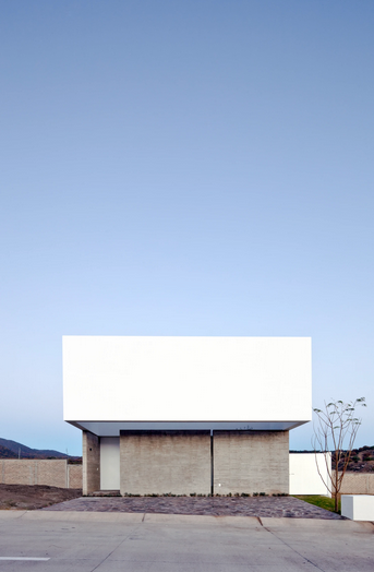 Casa para ver el cielo de COTAPAREDES arquitectos. Edificio minimalista con fachada blanca y base de concreto en un entorno despejado bajo cielo azul claro. Sensación de calma y simplicidad.