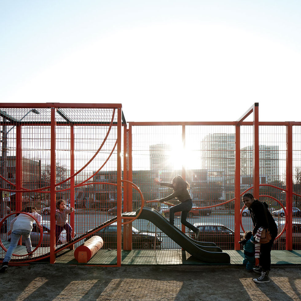 Niños juegan en un parque con estructuras rojas. El sol brilla intensamente detrás de edificios al fondo. Ambiente alegre y activo. en Revista FOCUS Latinoamerica