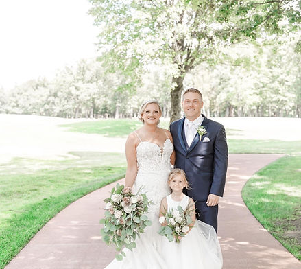 Bride and groom looking at camera with a little girl in a dress outside