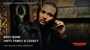 Bizzy Bone, wearing a black leather jacket and braids, sits in an ornate chair beside a fireplace.