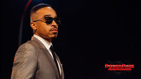 October London wears a gray suit and sunglasses against a dark stage backdrop, with the PowerPage logo at lower right.
