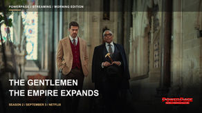 Theo James in a checked suit and Giancarlo Esposito in a dark suit walk side by side through a grand stone interior.