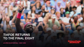 Frances Tiafoe smiles and raises one finger on court while wearing a pink and navy tennis shirt at the US Open.