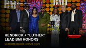 Nas in a green suit stands with six presenters on the colorful BMI R&B/Hip-Hop Awards stage