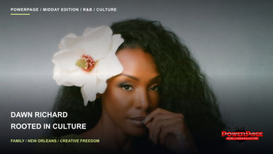 Dawn Richard poses against a gray background with wavy black hair, a white flower and a green blouse.