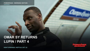 Omar Sy wears a black jacket and makes a hand gesture beneath a blue-and-white station sign.