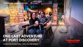 An adult crouches beside a child as they hold a rope on a wooden raft inside Port Discovery’s Adventure Expeditions, surrounded by rocks and an Egyptian-style setting.
