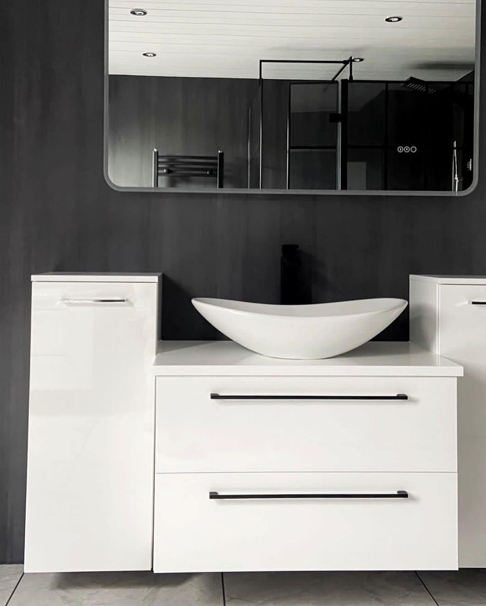 Freestanding sink basin on floating white cabinets and drawers under a large and wide rounded mirror opening up the space. With black walls creating a high contrast feeling for a sleek and modern bathroom that feels stylish and unique.
