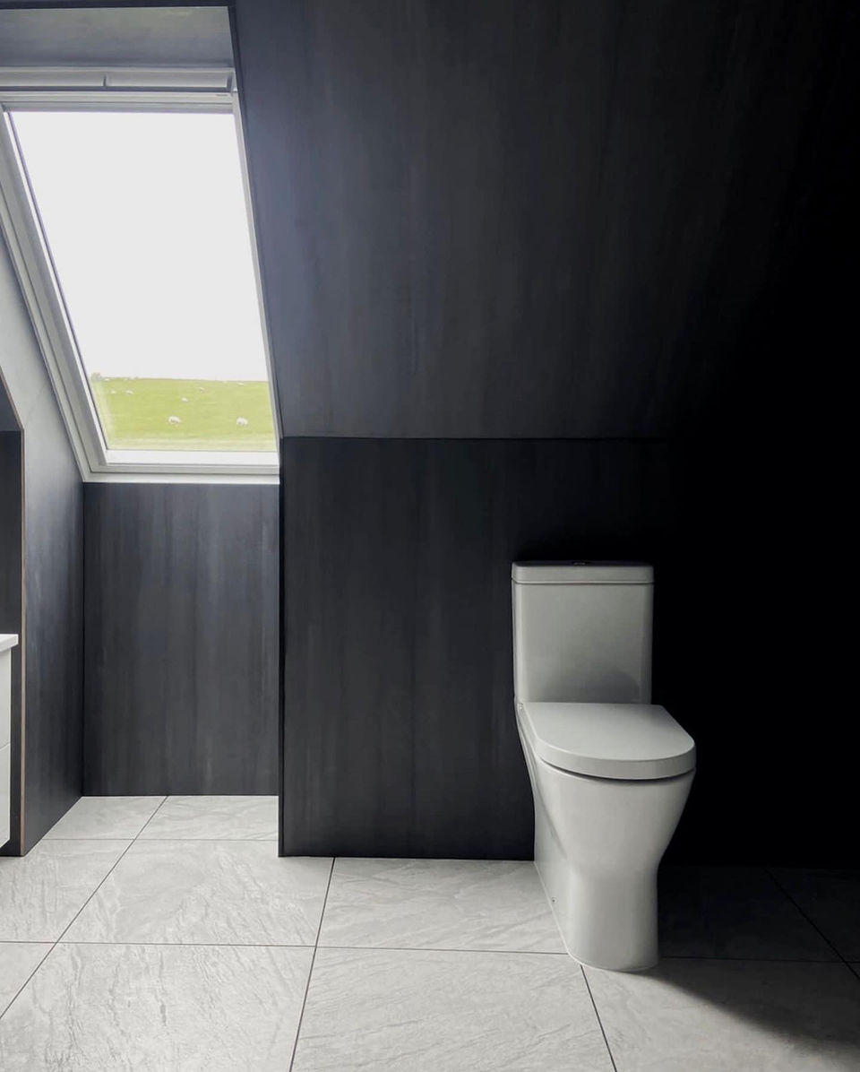 Dark walls, light locally sourced marble flooring with natural light pouring in through a velux window - the toilet stands along in strong contrast with the dark walls for a spacious and modern feeling bathroom renovation.