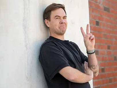 ein_mann_in_schwarzem_t-shirt_lehnt_lassig_an_einer_wand_und_zeigt_mit_einem_lacheln_das_p