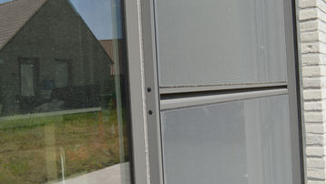 Close-up of gray window with house reflection; VINCK ramen & deuren.
