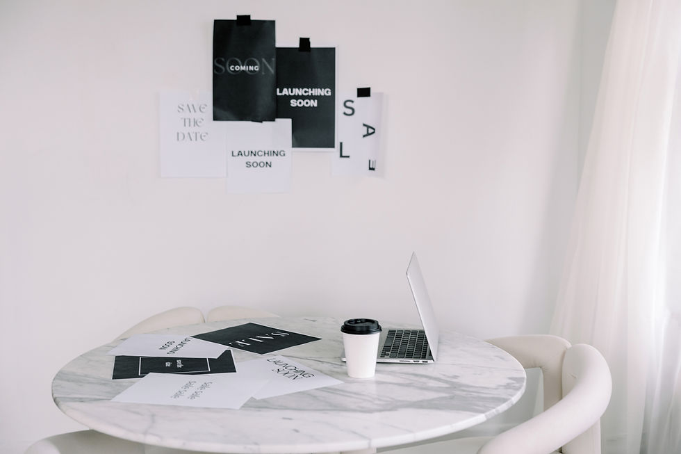 A marble table with a laptop and a coffee cup. Wall displays prints reading "Launching Soon" and "Sale" in a minimalist setting.