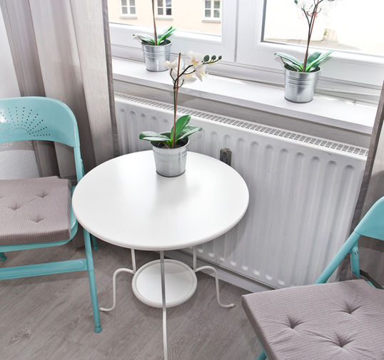Helle Sitzecke im zweiten Schlafzimmer des Apartments Paula in Augsburg mit einem kleinen weißen runden Tisch und zwei türkisfarbenen Stühlen am Fenster.