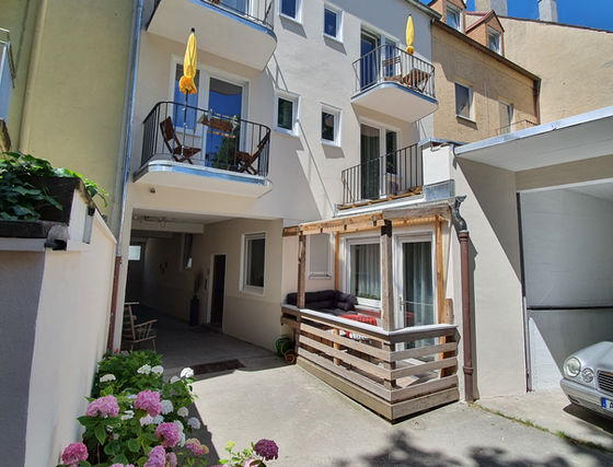Innenhof mit Balkonen, gelben Sonnenschirmen, Hortensien und überdachter Holzterrasse