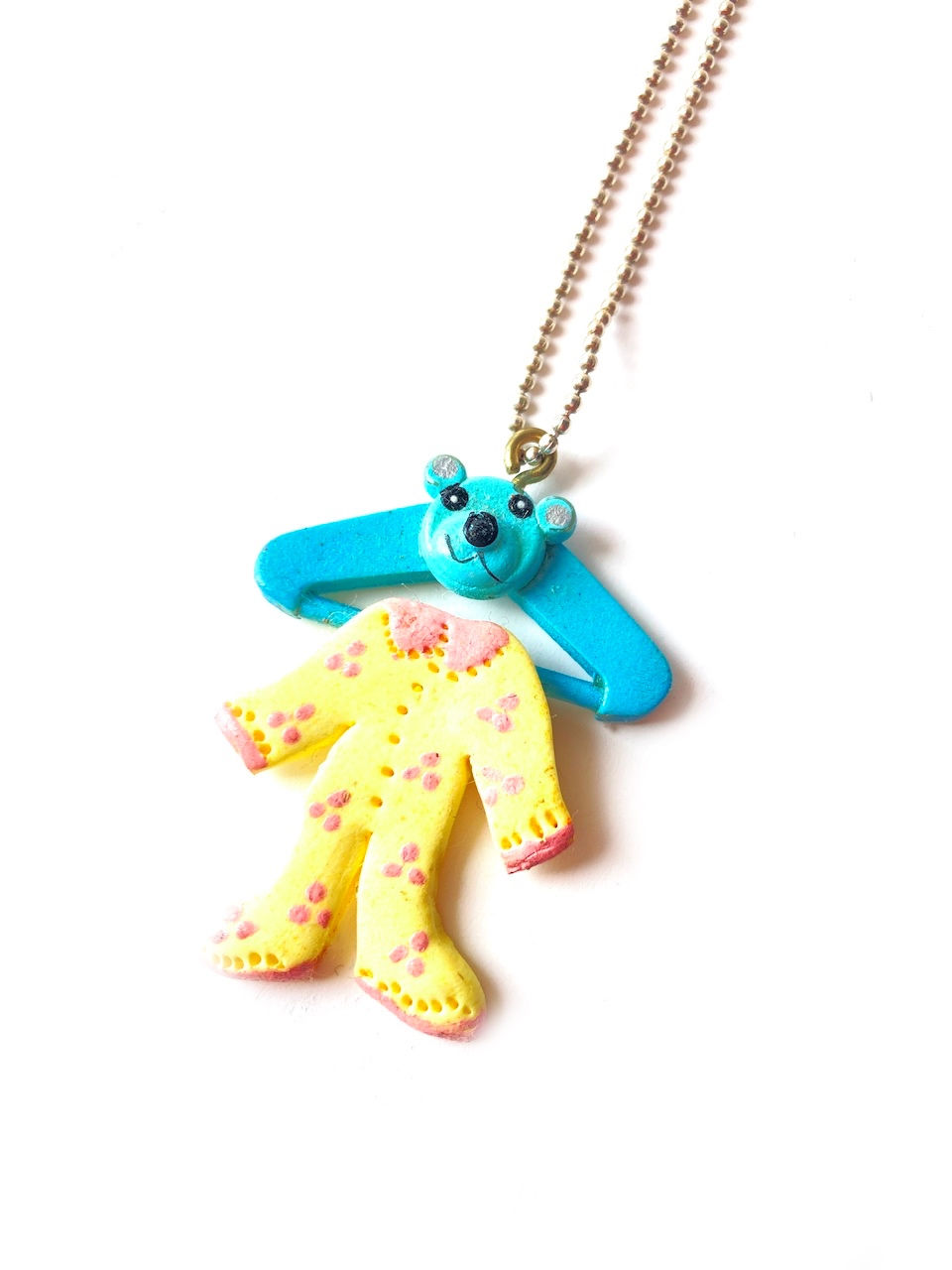 collier sautoir avec pyjama miniature de bébé jaune pastel sur cintre bleu avec ourson par The Sausage Jewels