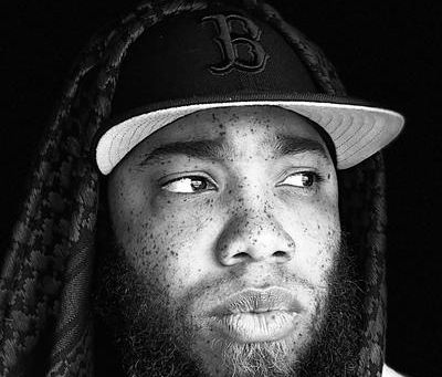 Black-and-white portrait of Virginia rapper IllyDaBanker wearing a Boston baseball cap and hooded sweatshirt while looking off-camera. The independent hip-hop artist is featured in THOP Fest's Artists to Watch spotlight for his single "It's Whatever."