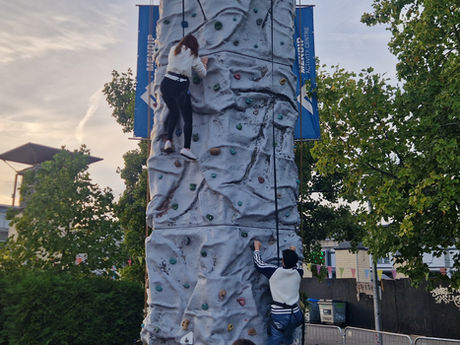 Two children scaling the Mendip Climbing Tower with harnesses on, silhouetted against a golden sunset sky.