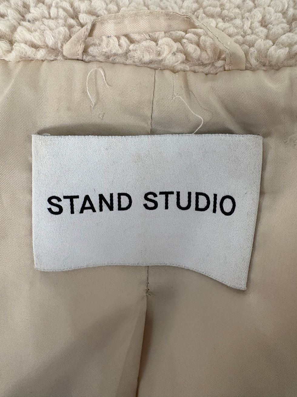 Miniaturbild: Nahaufnahme des weißen Etiketts mit dem Text STAND STUDIO auf cremefarbenem Hintergrund.