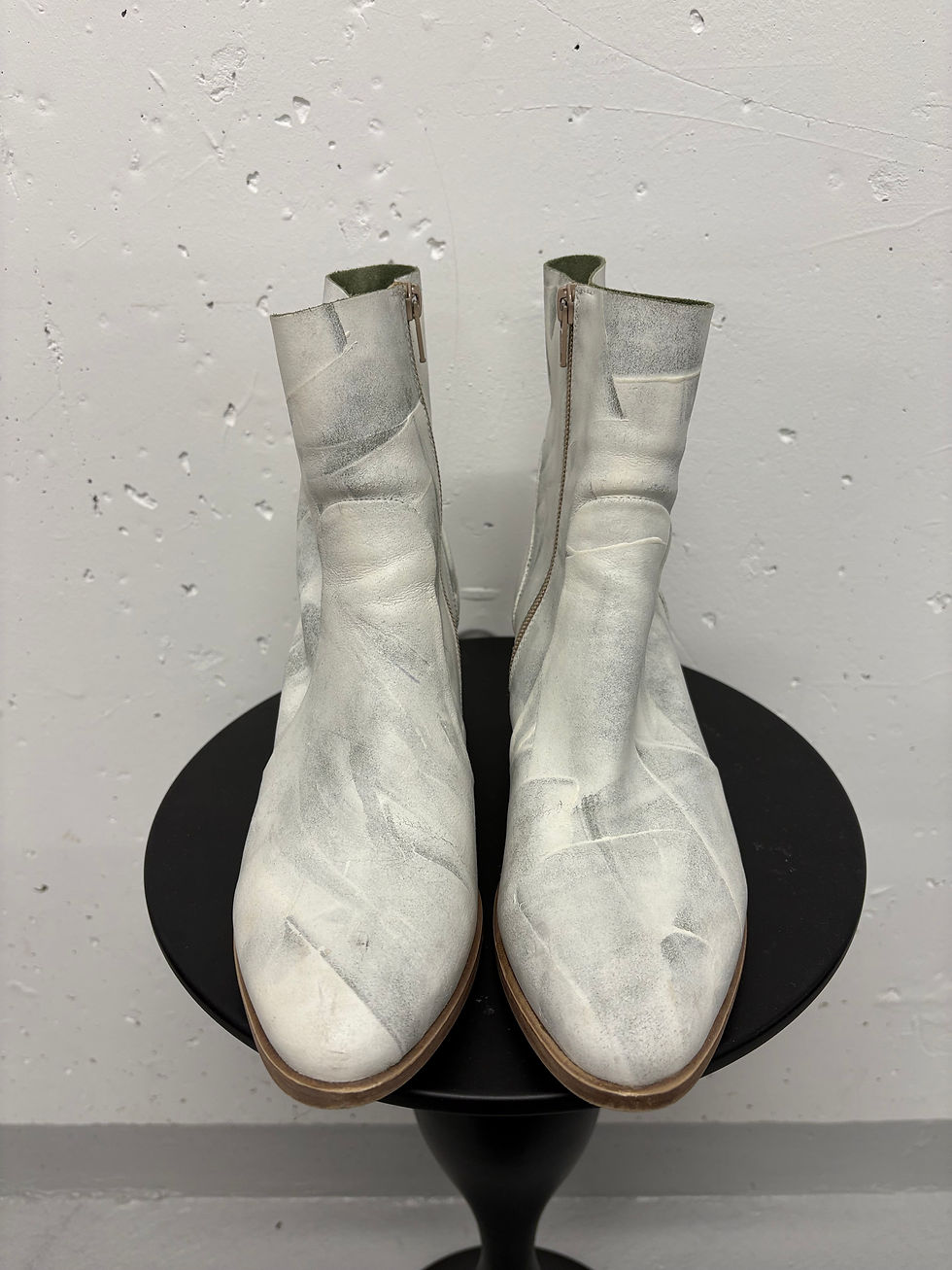 Miniaturbild: Weiße Lederstiefel stehen auf einem schwarzen Tisch vor einer grauen Wand.