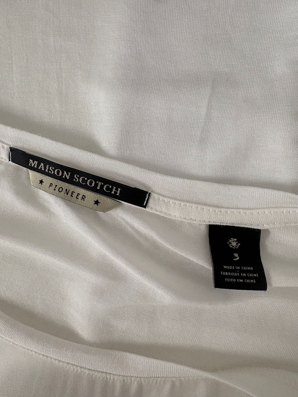 Miniaturbild: Nahaufnahme des weißen Hemdes mit Etikett: MAISON SCOTCH, PIONEER, Größe S.
