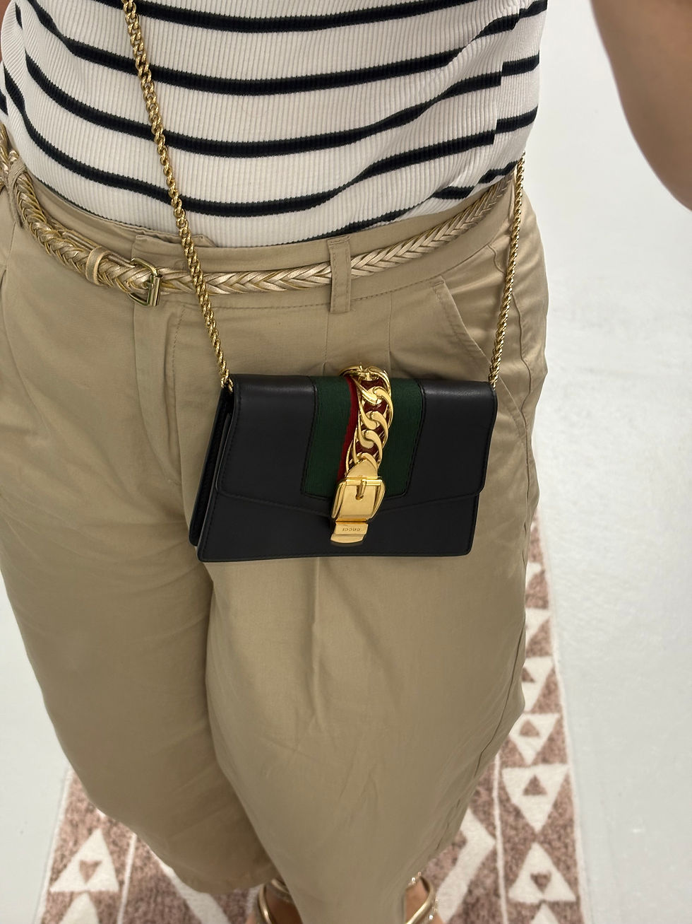 Miniaturbild: Dunkle Gucci Umhängetasche mit goldener Kette, braune Hose und Gürtel Detail.