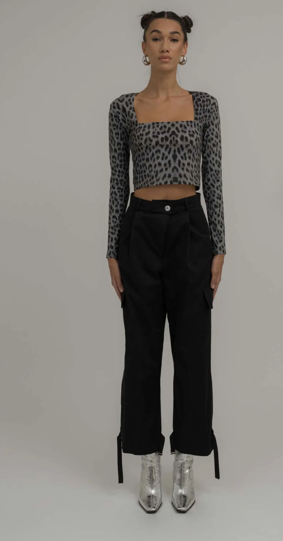 Frau in Leopard-Langarmshirt und schwarzer Hose vor hellem Hintergrund. 