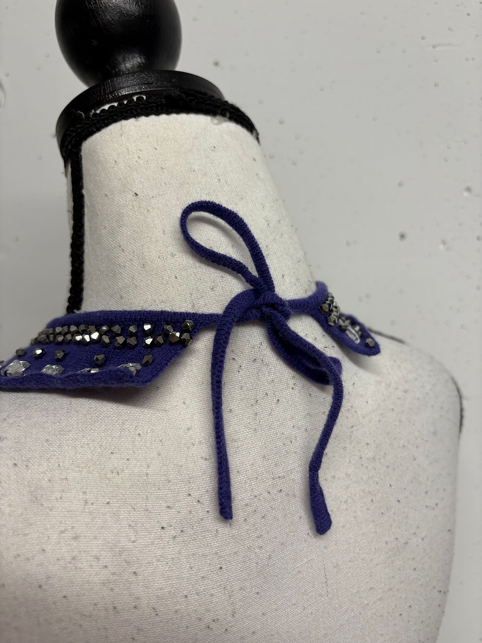 Miniaturbild: Blaues, mit Schmucksteinen besetztes Kragendetail auf einer Schaufensterpuppe mit Schleife.