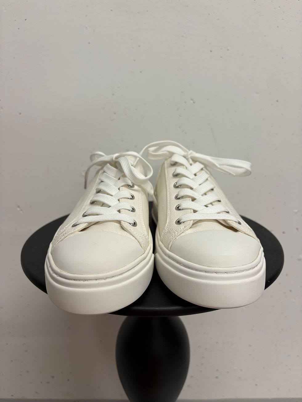 Miniaturbild: Paar weiße Ledersneakers auf einem schwarzen runden Tisch vor grauem Hintergrund.